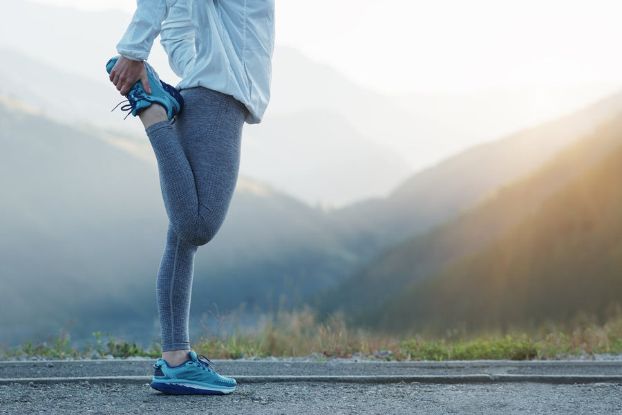 Läuferin dehnt sich vor dem Lauf im Morgenlicht in den Bergen