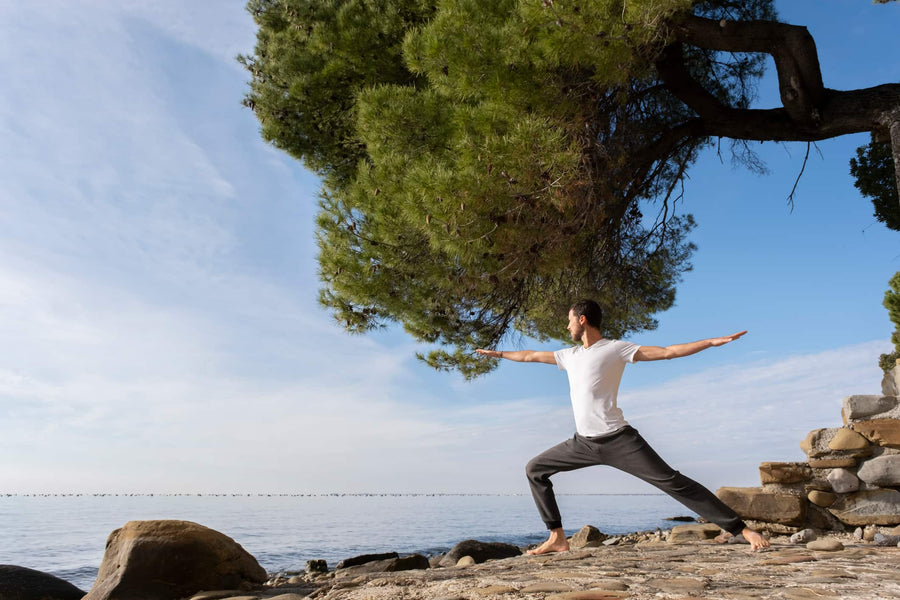 Mann in Yoga-Pose am Meer im Morgenlicht, ruhige Kraft